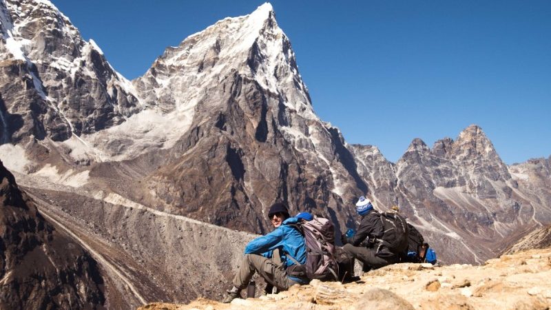 Group of travellers hiking along stairs to reach Everest Base Camp. White snowy peaks are seen in the distance.